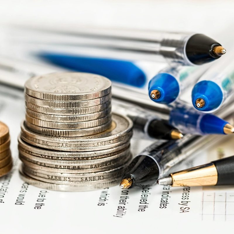 Monedas apiladas y bolígrafos sobre un estado de cuenta, curso de finanzas